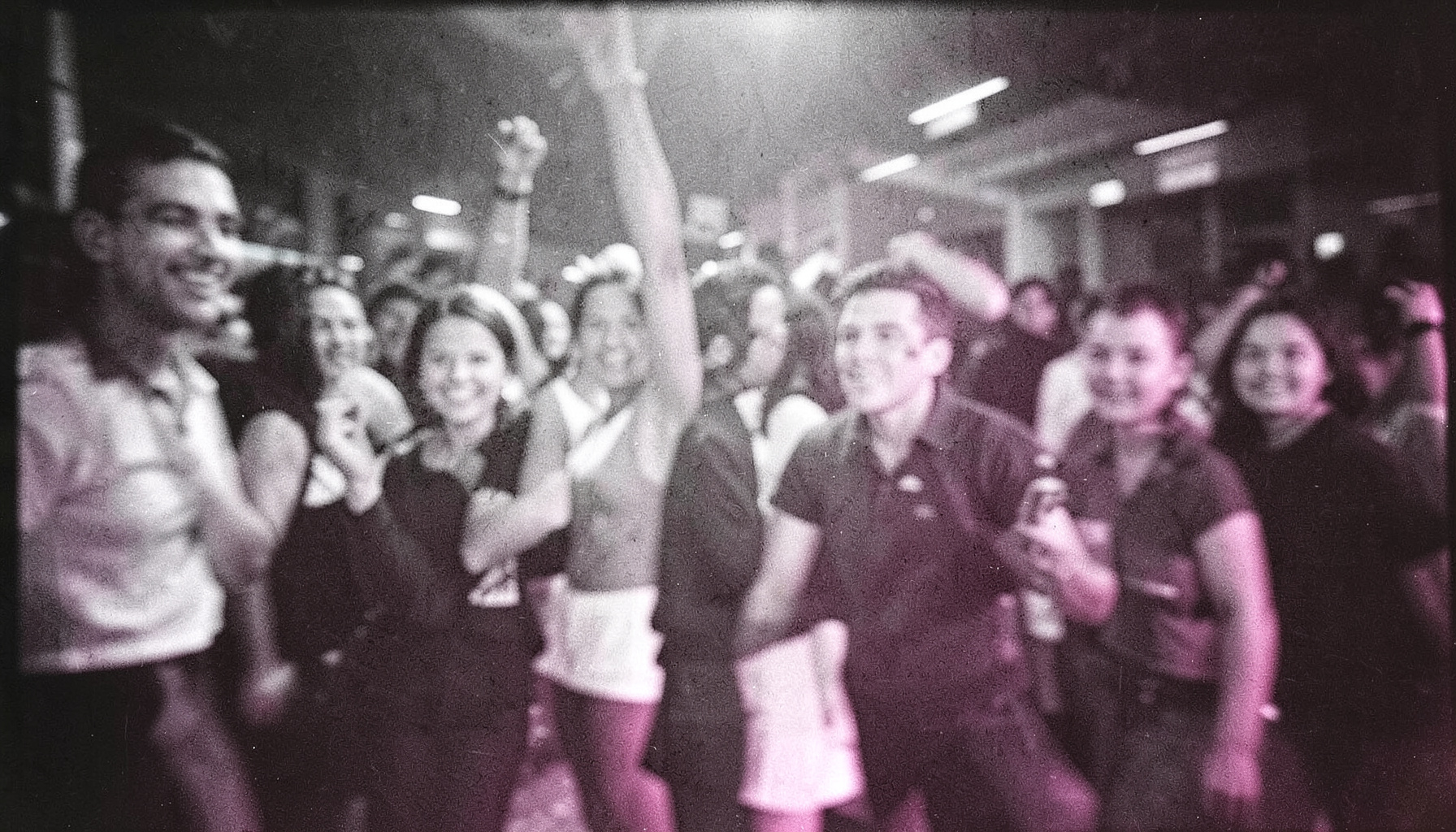 Black-and-white film photograph with visible grain, an event scene with motion blur and dramatic lighting, energetic and immersive mood