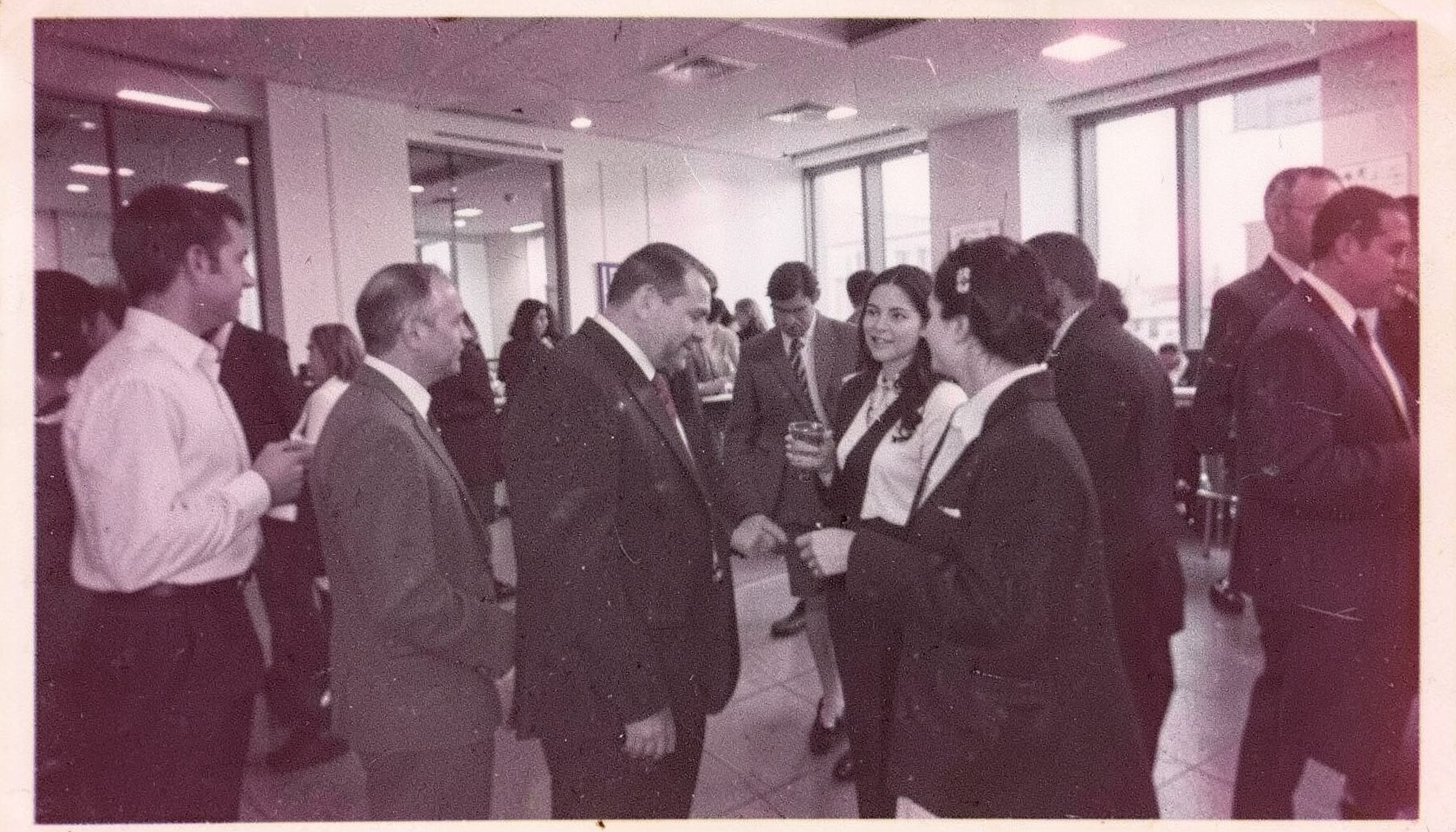 Grainy black-and-white film image of a corporate event interior with people in conversation, ambient light and candid atmosphere