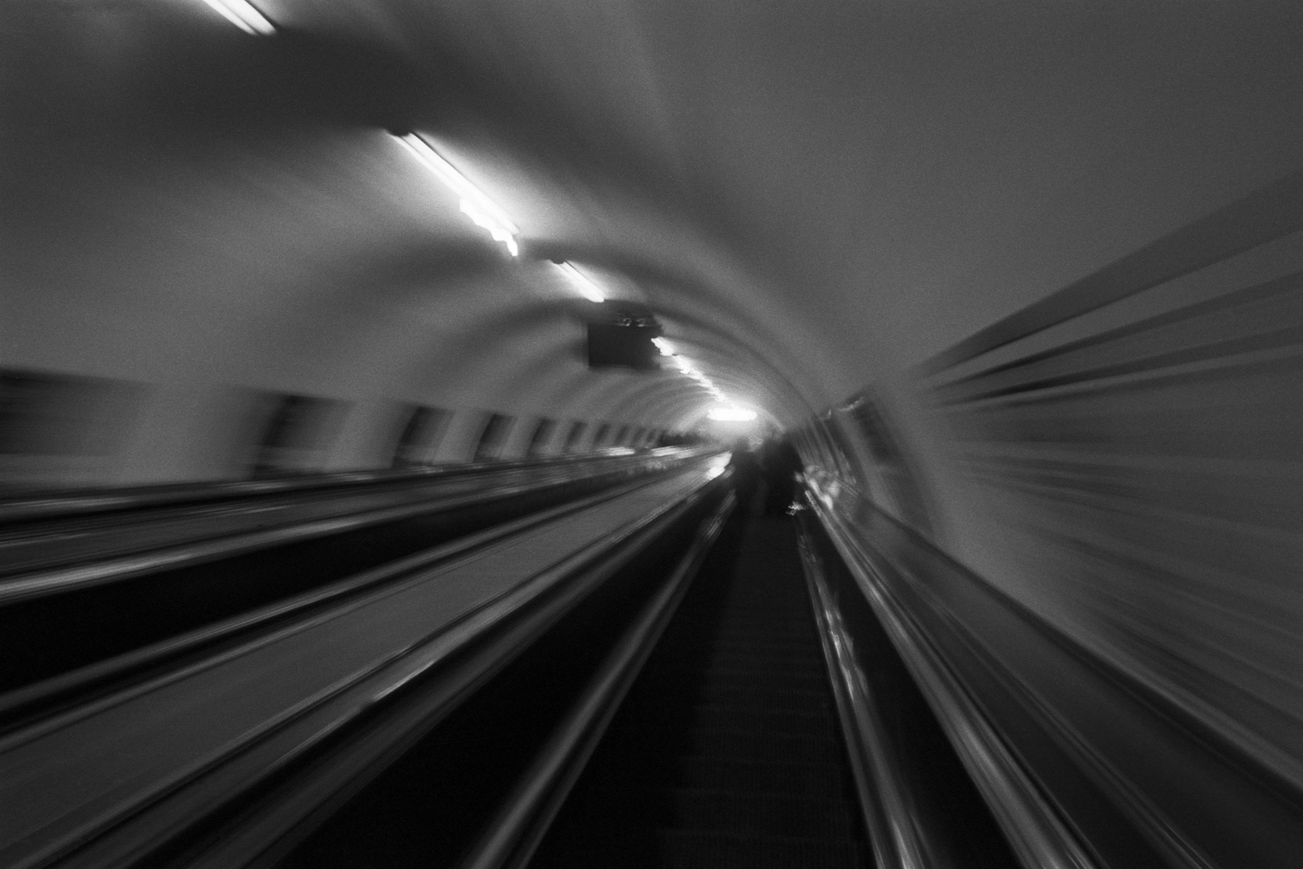 Motion-blurred black-and-white view down a curved tunnel with track lines and lights, dynamic and disorienting mood